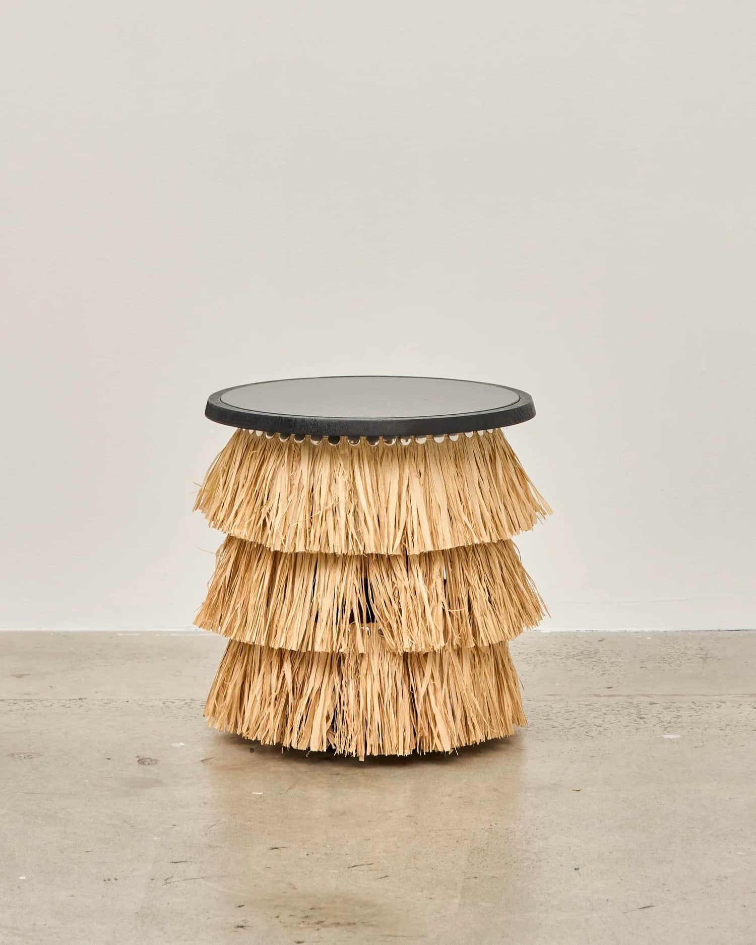 A compact side table featuring a dark, round tabletop supported by a tiered base made of natural, st… — 3D model