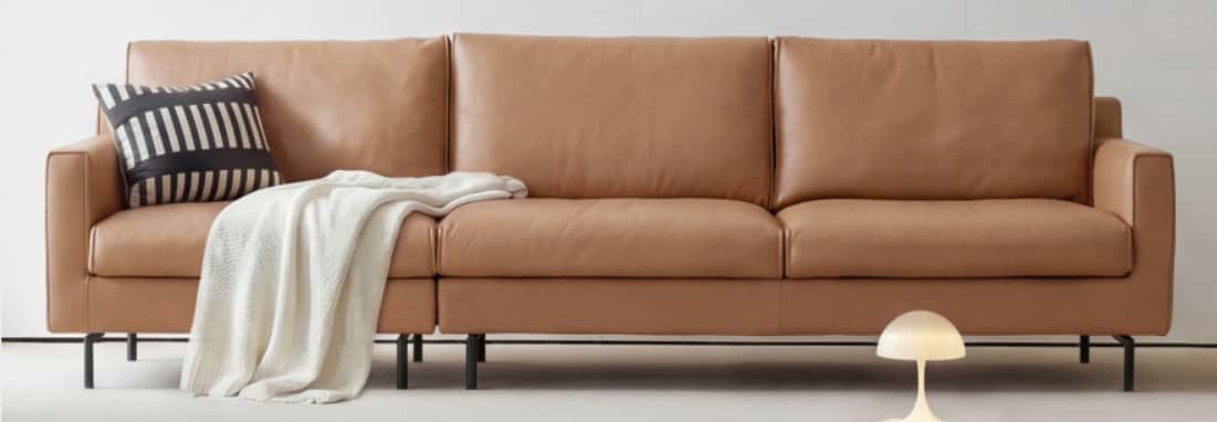 A modern three-seater sofa upholstered in tan-colored leather or faux leather, featuring a minimalis… — 3D model