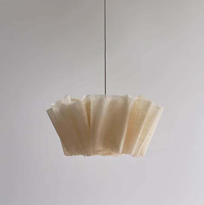 A modern pendant light featuring a cream-colored, pleated fabric shade, suspended by a dark cord. Th… — 3D model