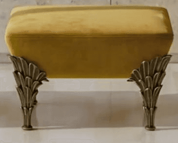 A rectangular ottoman featuring a plush mustard yellow velvet upholstered top and four ornate, leaf-… — 3D model