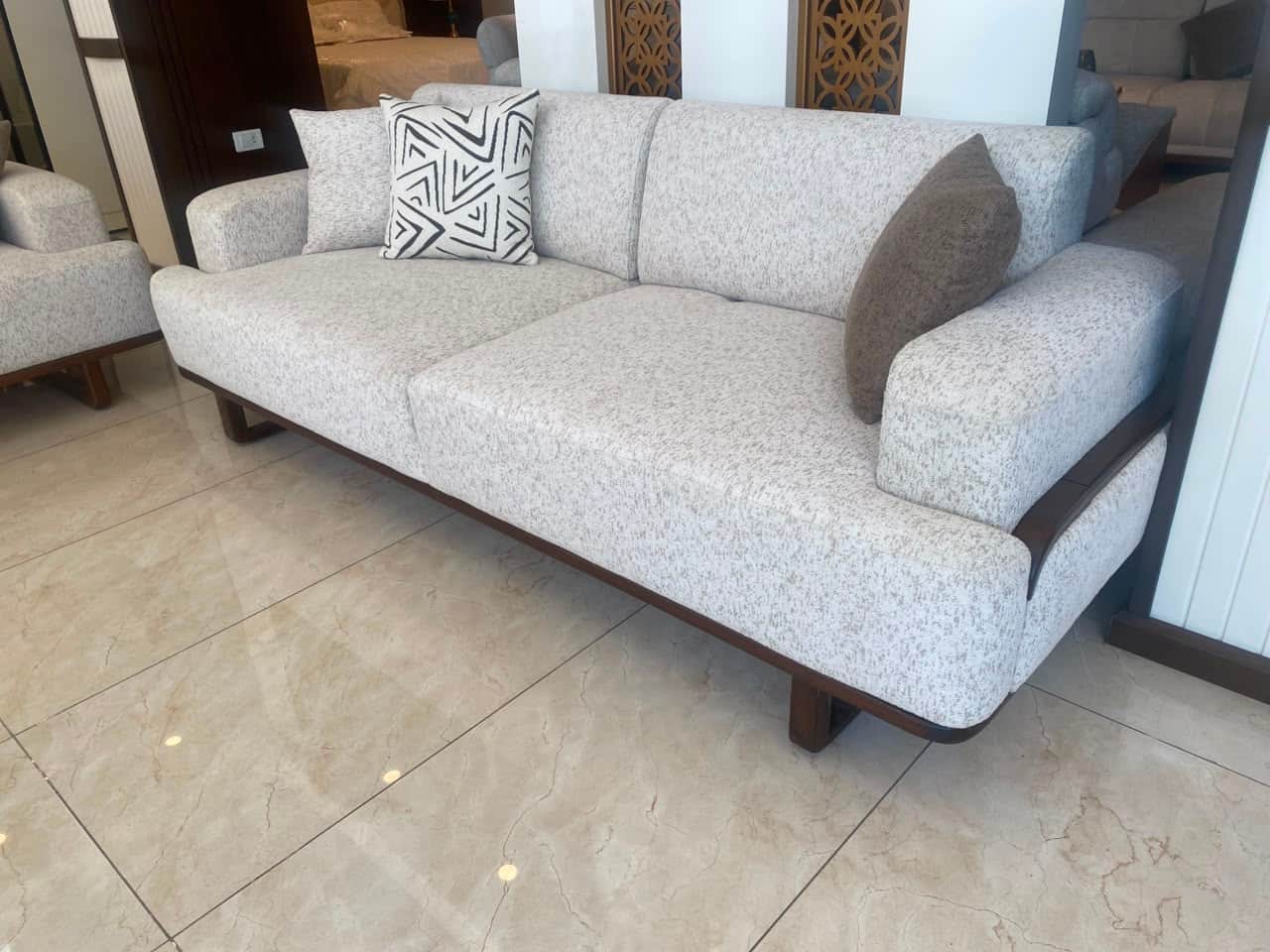 A contemporary two-seater sofa featuring light grey textured fabric upholstery and a visible dark wo… — 3D model