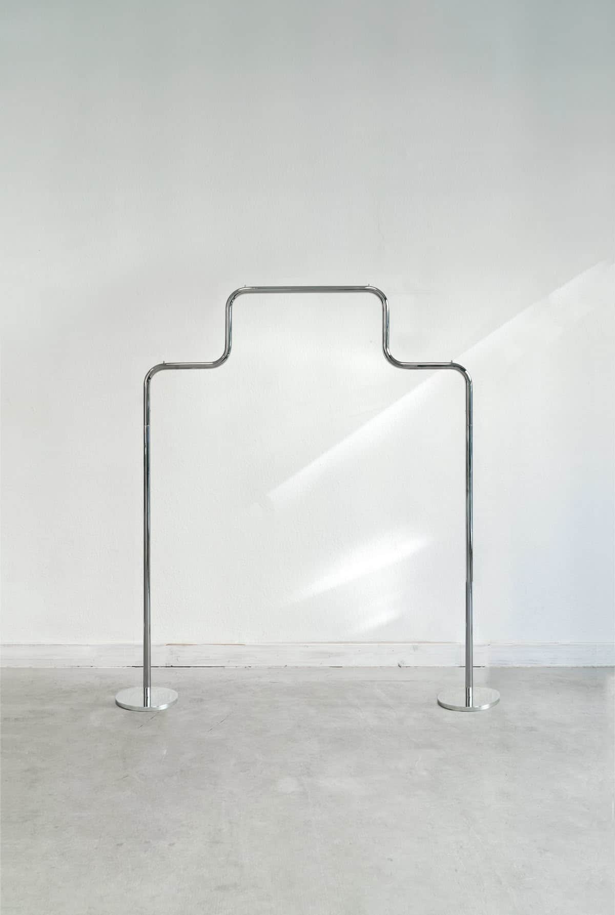 A minimalist, freestanding garment rack made of polished chrome or silver-toned metal, featuring a c… — 3D model