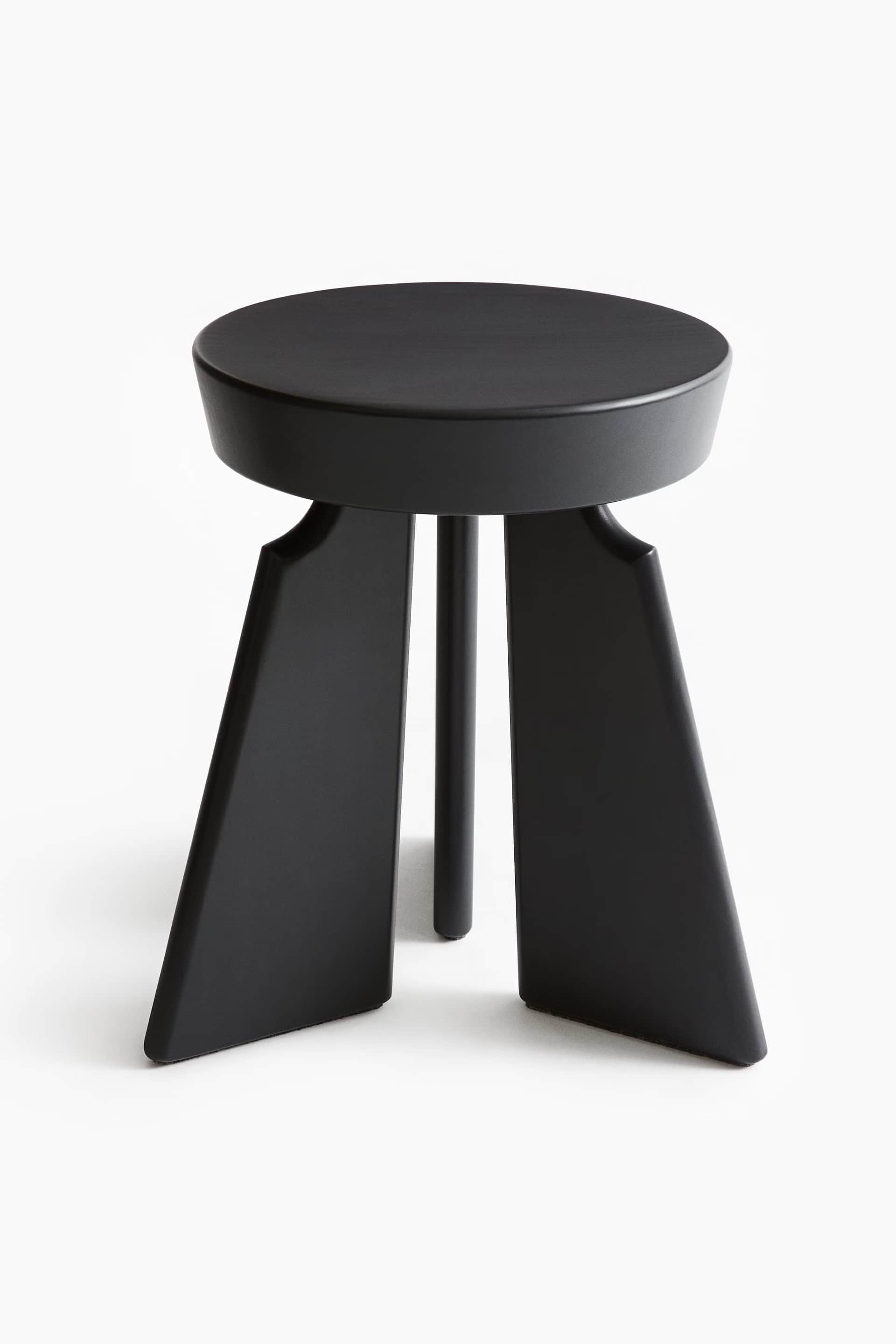 A minimalist black three-legged stool featuring a round, thick seat and a distinctive leg design wit… — 3D model