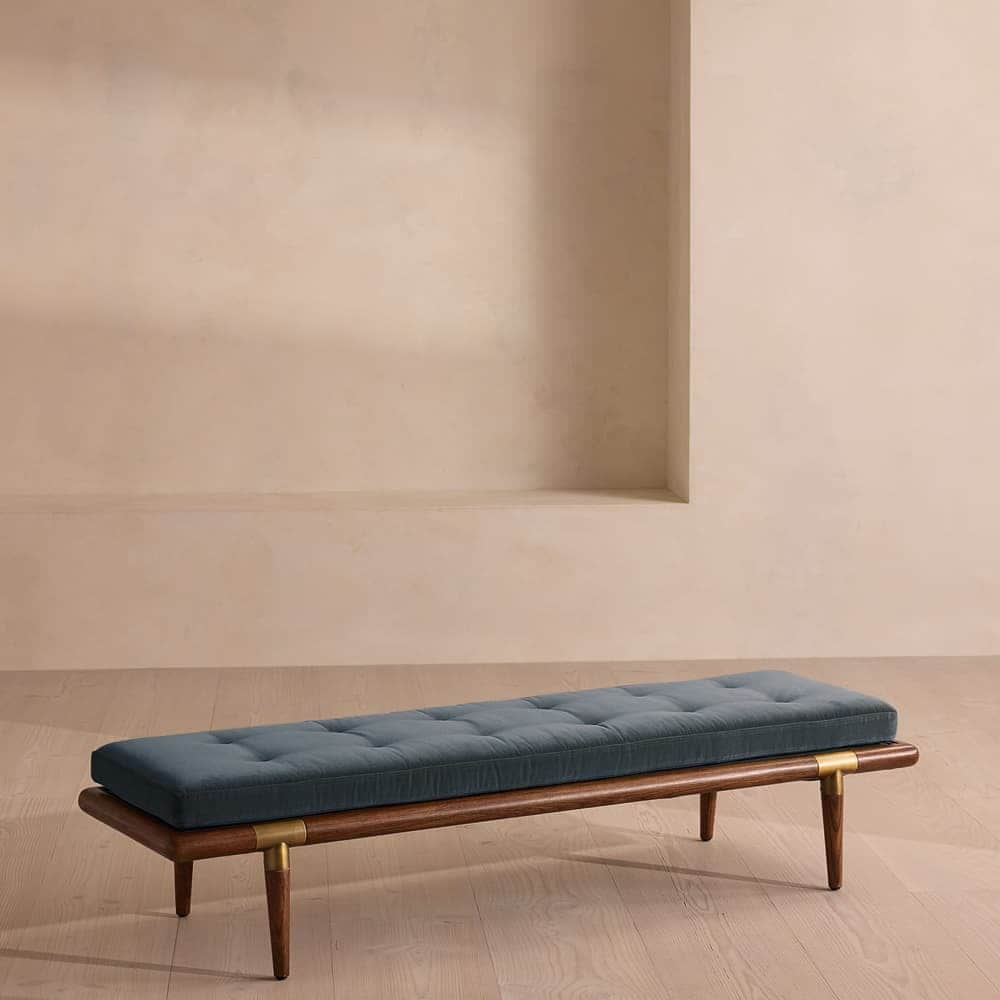 A long, upholstered bench with a wooden frame. The seat is tufted and covered in a dark, possibly bl… — 3D model