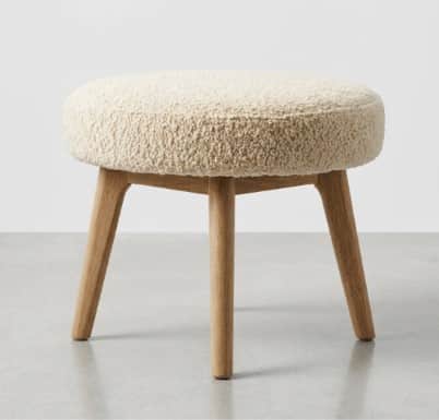 A round stool with a plush, textured seat and three tapered wooden legs. — 3D model