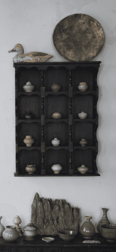 A black, wall-mounted display shelf featuring a tiered structure with scalloped side panels and turned wooden spindles. The shelf unit holds various small, decorative ceramic pots or vases across its multiple levels, designed for showcasing small collectibles. — 3D model