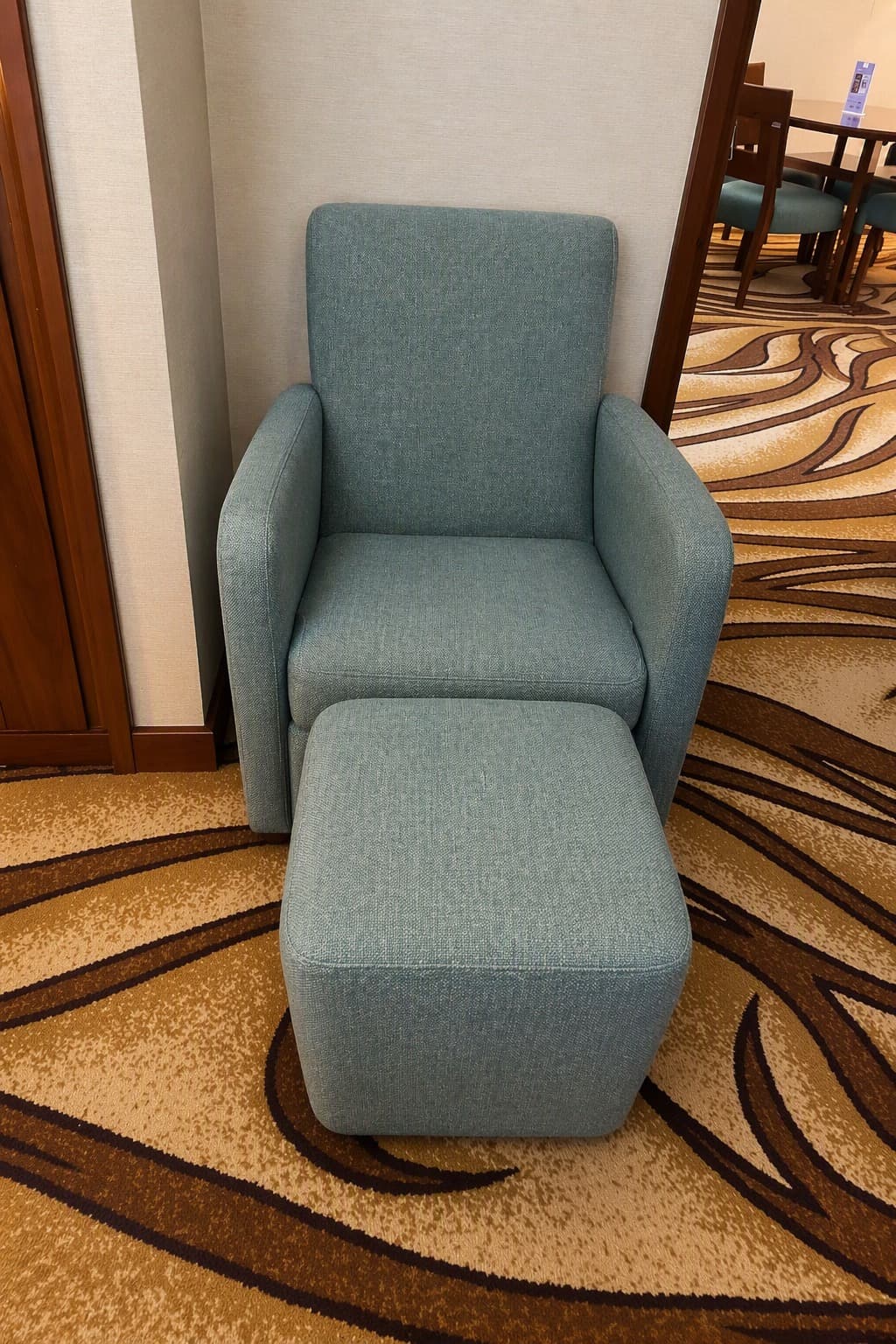 An upholstered armchair and a matching ottoman are presented in a contemporary style. Both pieces are covered in a textured, light teal fabric and feature a squared-off silhouette with soft, rounded edges. The armchair has integrated, padded arms and a straight back. The ottoman is a simple rectangular block, designed to serve as a footrest or additional seating. — 3D model