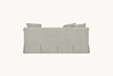 A light-colored, slipcovered sofa with a tailored skirt featuring pleats. It has plush seat and back cushions, with three throw pillows arranged on the back. The sofa arms are slightly curved. — 3D model