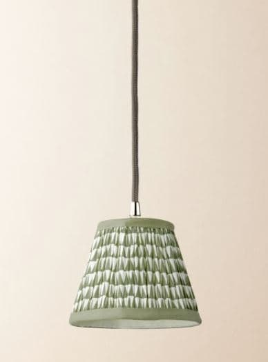 A mini pendant light featuring a conical shade made of pleated fabric. The fabric displays a geometric pattern in sage green and white, with a solid sage green trim at the top and bottom edges. The shade is suspended by a textile-wrapped cord in a dark gray color, connecting to a small silver-toned metal fitting at the top of the shade. The overall design suggests a contemporary or artisanal aesthetic. — 3D model
