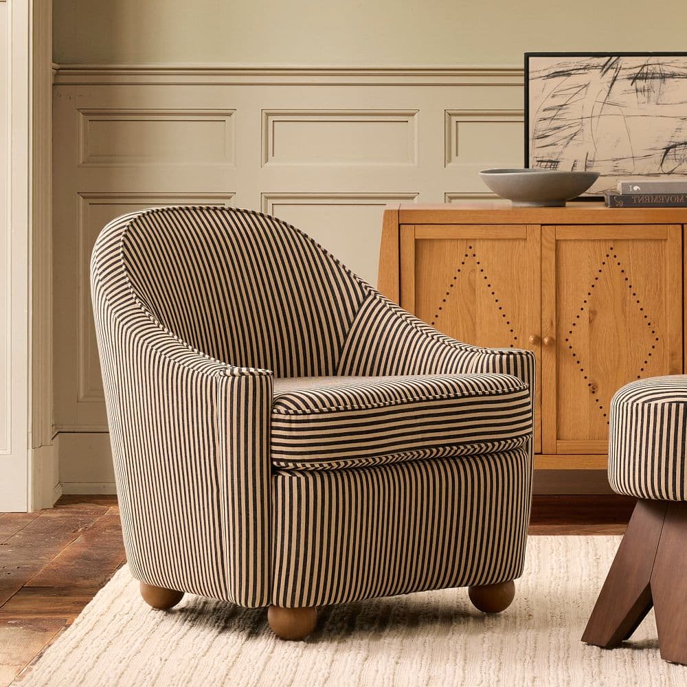 A compact armchair upholstered in fabric with a black and tan vertical stripe pattern. It features a rounded back, integrated armrests, and a seat cushion. The chair is supported by four short, cylindrical wooden legs. — 3D model
