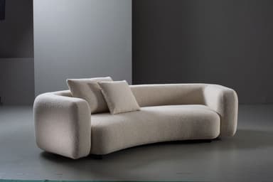 A contemporary, low-profile sofa upholstered in a cream-colored boucle fabric, featuring soft, rounded edges and a subtly curvilinear form, accompanied by two matching throw pillows. — 3D model
