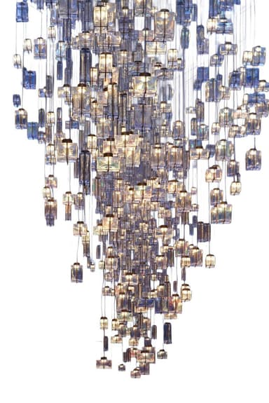 A grand, multi-tiered chandelier featuring numerous individual lighting elements suspended at varying heights to create a dramatic cascading effect. Each element consists of a rectangular block of textured or molded glass, appearing in shades of clear, blue, and amber, encasing an internal light source. The overall form tapers downwards, presenting a dynamic and luxurious illuminated sculpture. — 3D model