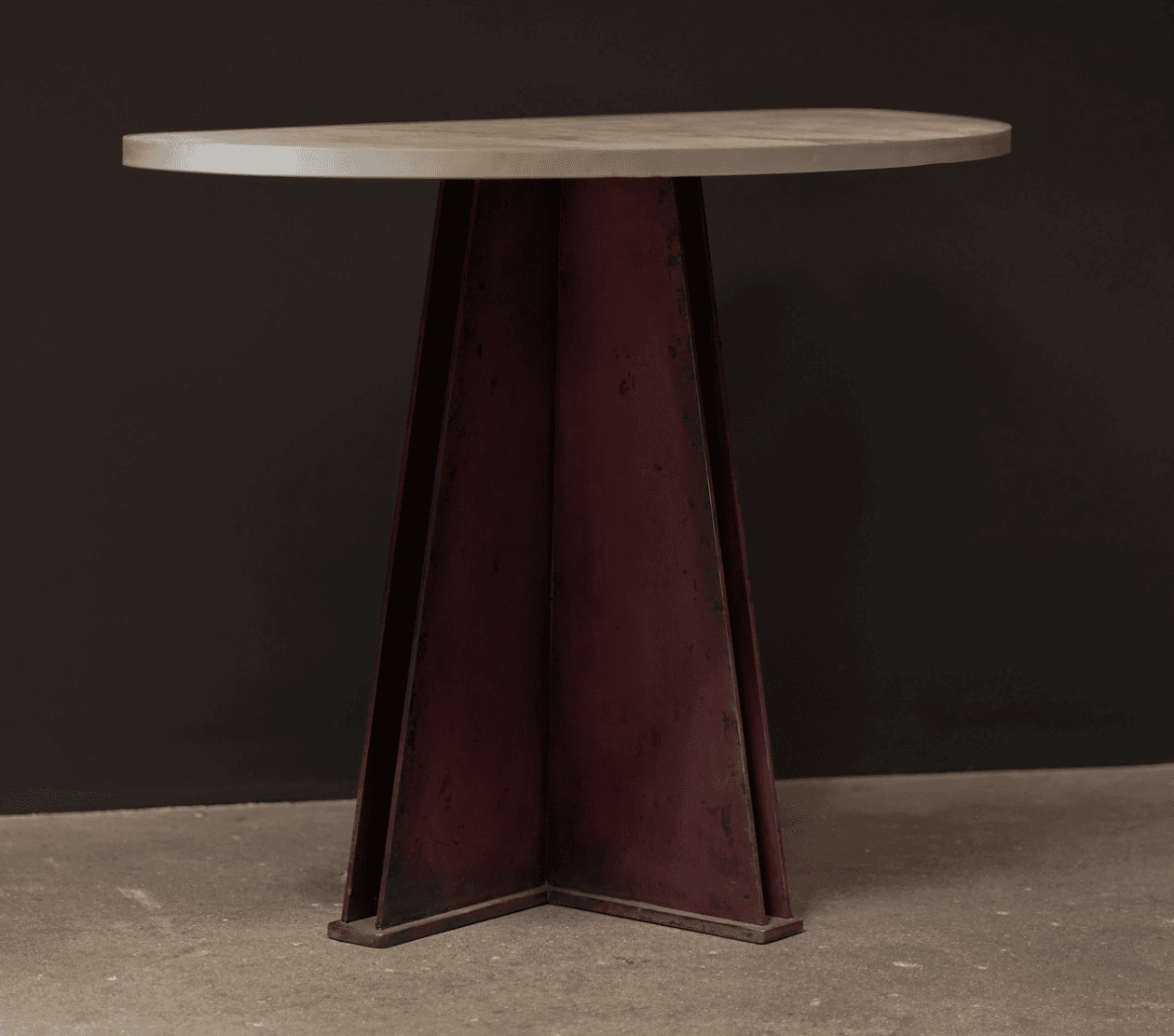 A contemporary console table featuring a grey concrete half-moon shaped top and a sculptural, angular metal pedestal base with a distressed dark red/rust finish. The base is composed of several tapering metal sheets forming a substantial, inverted-pyramid-like structure. — 3D model