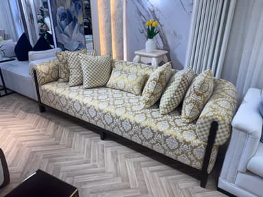 A traditional, ornate upholstered sofa featuring a gold and cream damask pattern, rolled armrests, dark wood frame, and multiple coordinating throw pillows. — 3D model
