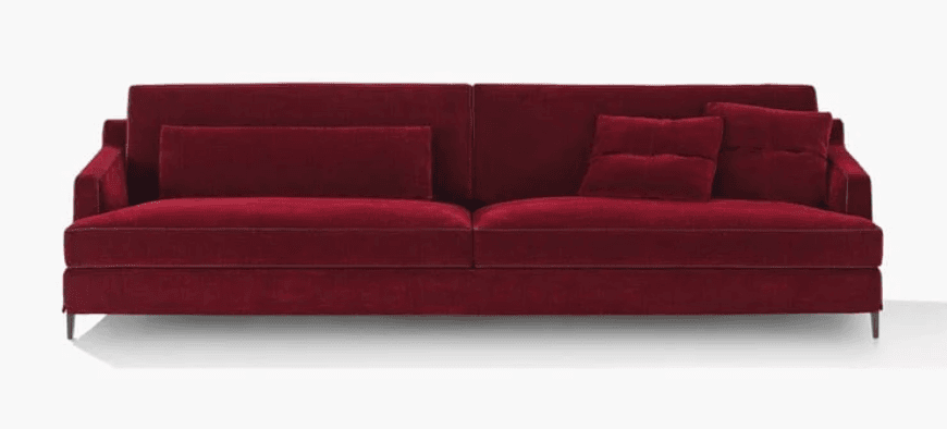 A contemporary three-seater sofa upholstered in a deep red, possibly velvet or a similar plush fabric. It features a clean-lined design with a low profile, thin piping along the edges of the seat and back cushions, and slightly tapered arms. Two throw pillows are included: one rectangular lumbar pillow placed on the left side of the backrest, and two square pillows on the right side, with one slightly overlapping the other. The sofa is supported by slender, dark-colored legs. — 3D model