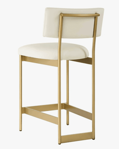 A modern bar stool featuring a gold-finished metal frame with a rectangular footrest and four legs. The seat and backrest are upholstered in a light, off-white or cream fabric/leatherette. The backrest is gently curved, and the frame extends up to support it. The overall design is sleek and contemporary. — 3D model