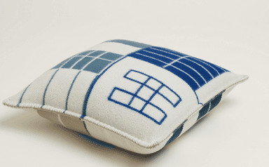A square cushion with a geometric pattern. The pattern consists of blocks of blue and white with white grid lines. The edges are finished with a contrasting stitch. — 3D model