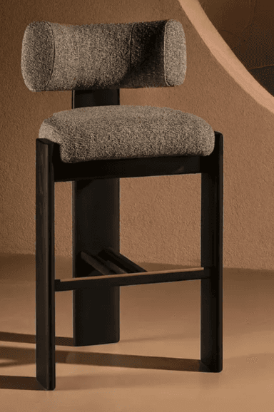 A modern bar stool featuring a curved backrest and seat upholstered in a textured grey fabric. The base and frame are constructed from black finished wood, with a subtle brass accent on the footrest. — 3D model
