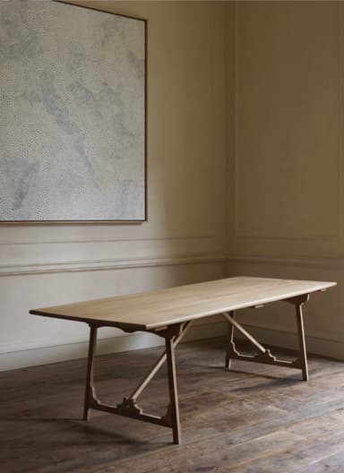 A light-colored wooden dining table featuring a rectangular tabletop supported by two distinctive trestle-style bases. The wood exhibits a fine grain, suggesting materials like oak or ash, contributing to a natural and minimalist aesthetic. The trestle bases are designed with angular supports and a horizontal crossbar, providing stability and a visually appealing structural element. — 3D model