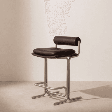 A modern bar stool featuring a tubular metal frame with a brushed finish, brown leather upholstery on the seat, and a cylindrical backrest. The seat is padded and includes button-tufting or quilting details. An integrated footrest is part of the metal frame. — 3D model