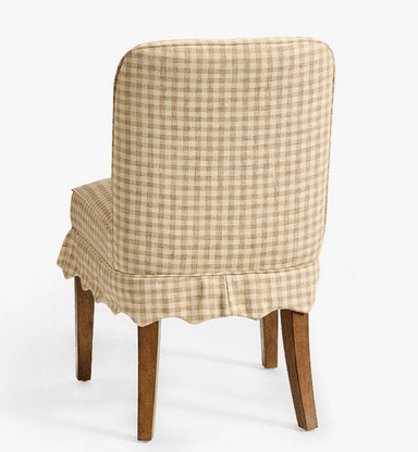 A fully upholstered dining chair featuring a beige and white gingham check pattern. The chair has a tall, slightly curved backrest and a padded seat. A decorative scalloped skirt covers the lower part of the seat frame, partially concealing the upper portion of the four tapered wooden legs. The design suggests a blend of traditional and country-style aesthetics. — 3D model