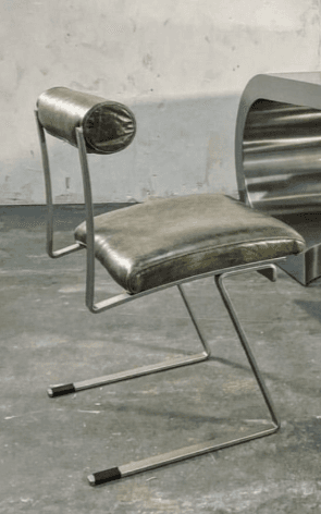 A modern dining chair with a cantilever base. The seat and backrest are upholstered in a dark olive-green material. The frame is made of tubular metal, possibly steel or aluminum, with a matte silver finish. The backrest is a single, cylindrical cushion attached to the frame. — 3D model