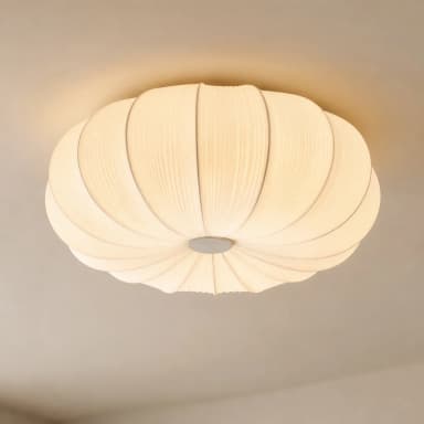 An off-white or cream-colored ceiling light fixture featuring a pleated fabric shade that creates a soft, organic, and somewhat pumpkin-like silhouette. The light is mounted close to the ceiling with a small, discreet base in a metallic finish, likely gray or bronze. The pleats are evenly distributed, contributing to a diffused and ambient light output. The overall design appears contemporary and minimalist. — 3D model