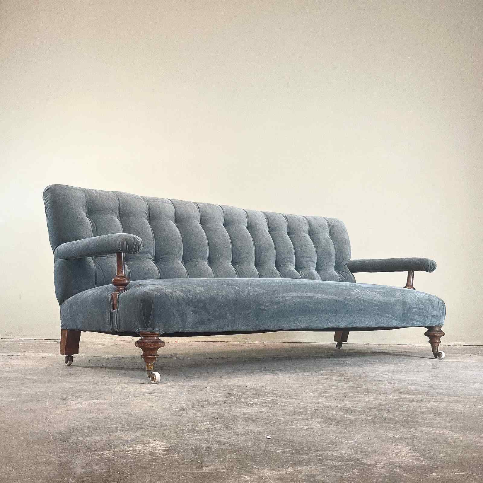 A vintage-style sofa with a tufted backrest and seat. It features upholstered armrests supported by wooden elements and sits on turned wooden legs with casters on the front two legs. — 3D model