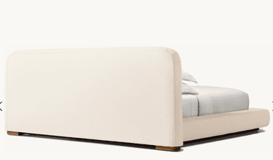 A low-profile bed frame with a rounded headboard and platform base, upholstered in a textured, light-colored fabric. The bed is dressed with white bedding, including two pillows stacked neatly. — 3D model