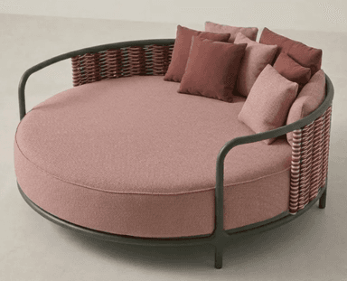 A contemporary outdoor circular daybed featuring a dark green metal frame, a woven backrest in variegated tones of pink and brown, and a large round cushion with multiple throw pillows in shades of pink and rose. The base cushion and some pillows have a textured fabric finish, while others are solid. — 3D model