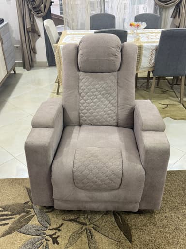 A light grey, upholstered, single-seat reclining chair with quilted accents on the backrest and seat. It features wide, padded armrests and a segmented backrest with an integrated headrest, currently shown in a reclined position. — 3D model