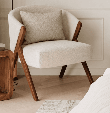An upholstered armchair featuring a rounded barrel-back design, covered in off-white bouclé fabric, with an exposed dark wood frame that forms the armrests and splayed legs. Includes a matching lumbar pillow. — 3D model