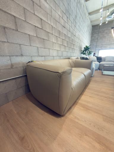 A modern two-seater sofa upholstered in light beige leather, featuring a plush, rounded design with a low profile. The backrest shows subtle vertical channeling, and the two individual seat cushions have a gentle tufted appearance. The overall form is volumetric and fluid. — 3D model