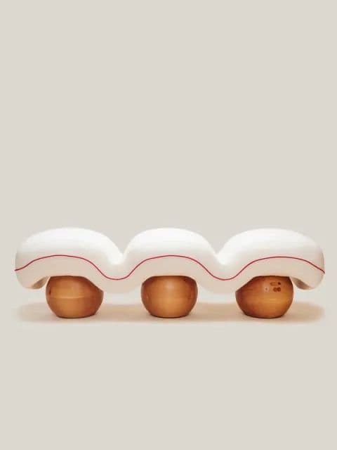 A contemporary bench with a wavy, bulbous white upholstered seat. The seat is supported by three spherical wooden legs with a natural finish. A thin red line accents the underside of the upholstered seat, following its undulating form. — 3D model