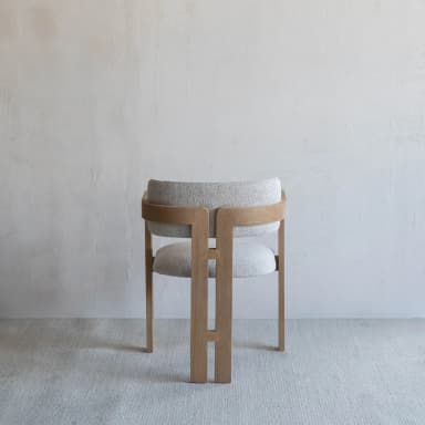 A contemporary dining chair featuring a light-toned wooden frame and light gray upholstered seat and backrest. The backrest is gently curved, providing integrated armrests as part of the overall wooden structure. The rear legs feature distinctive H-shaped vertical cutouts, adding to its modern aesthetic. — 3D model