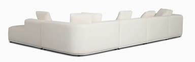 A large, contemporary modular U-shaped sectional sofa upholstered in a cream-colored fabric, featuring soft, rounded edges and a low-profile design, complete with multiple back cushions. — 3D model