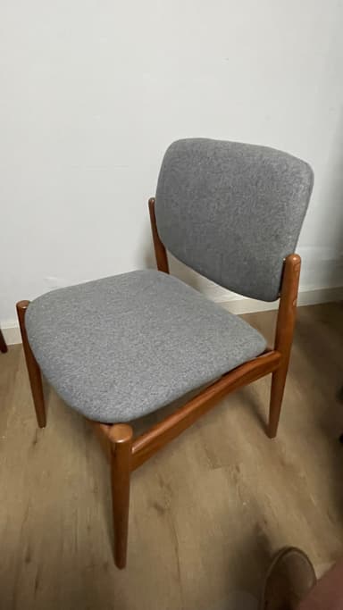 An armless dining chair with a visible solid wood frame and upholstered seat and back. The wood has a warm, medium-brown tone, and the upholstery is a light gray fabric. The chair features a minimalist design with tapered legs and a gently curved backrest, characteristic of Scandinavian or Mid-Century Modern aesthetics. The frame appears sturdy with clean lines. — 3D model