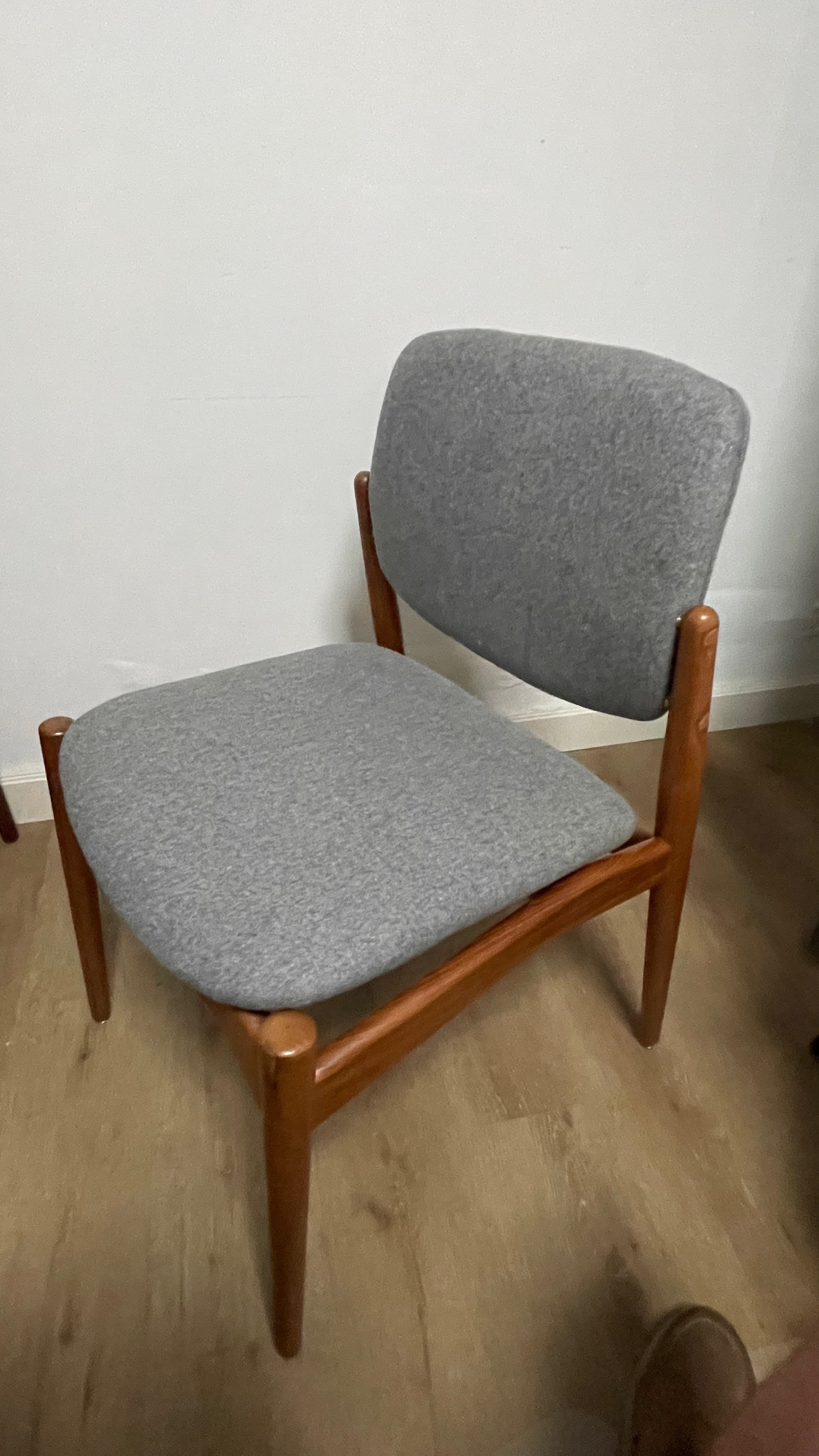 An armless dining chair with a visible solid wood frame and upholstered seat and back. The wood has a warm, medium-brown tone, and the upholstery is a light gray fabric. The chair features a minimalist design with tapered legs and a gently curved backrest, characteristic of Scandinavian or Mid-Century Modern aesthetics. The frame appears sturdy with clean lines. — 3D model