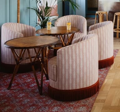 A round, upholstered accent chair with a curved backrest and armrests integrated into the seat. The chair is covered in a fabric with a repeating chevron or feather-like pattern in neutral tones. A decorative fringe in a dark brown or rust color encircles the base of the chair. — 3D model