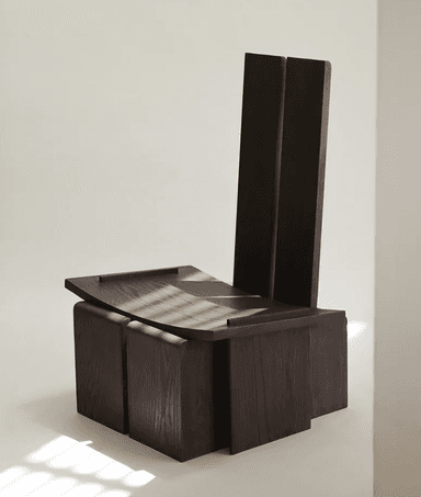 A dark wood chair featuring a highly geometric and architectural design. The backrest is composed of two tall, separated rectangular panels. The seat is a broad, flat panel that appears to float above a solid, angular base constructed from interconnected wooden blocks. The wood has a visible grain and a deep, rich brown finish. — 3D model