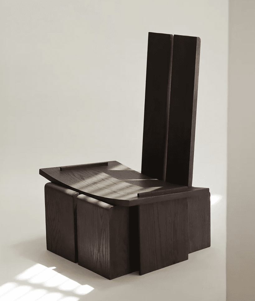 A dark wood chair featuring a highly geometric and architectural design. The backrest is composed of two tall, separated rectangular panels. The seat is a broad, flat panel that appears to float above a solid, angular base constructed from interconnected wooden blocks. The wood has a visible grain and a deep, rich brown finish. — 3D model