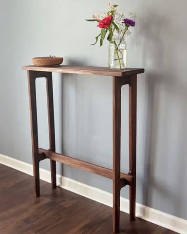 A minimalist, slimline console table crafted from dark walnut wood, featuring a rectangular top and integrated leg structures connected by a horizontal stretcher bar. — 3D model