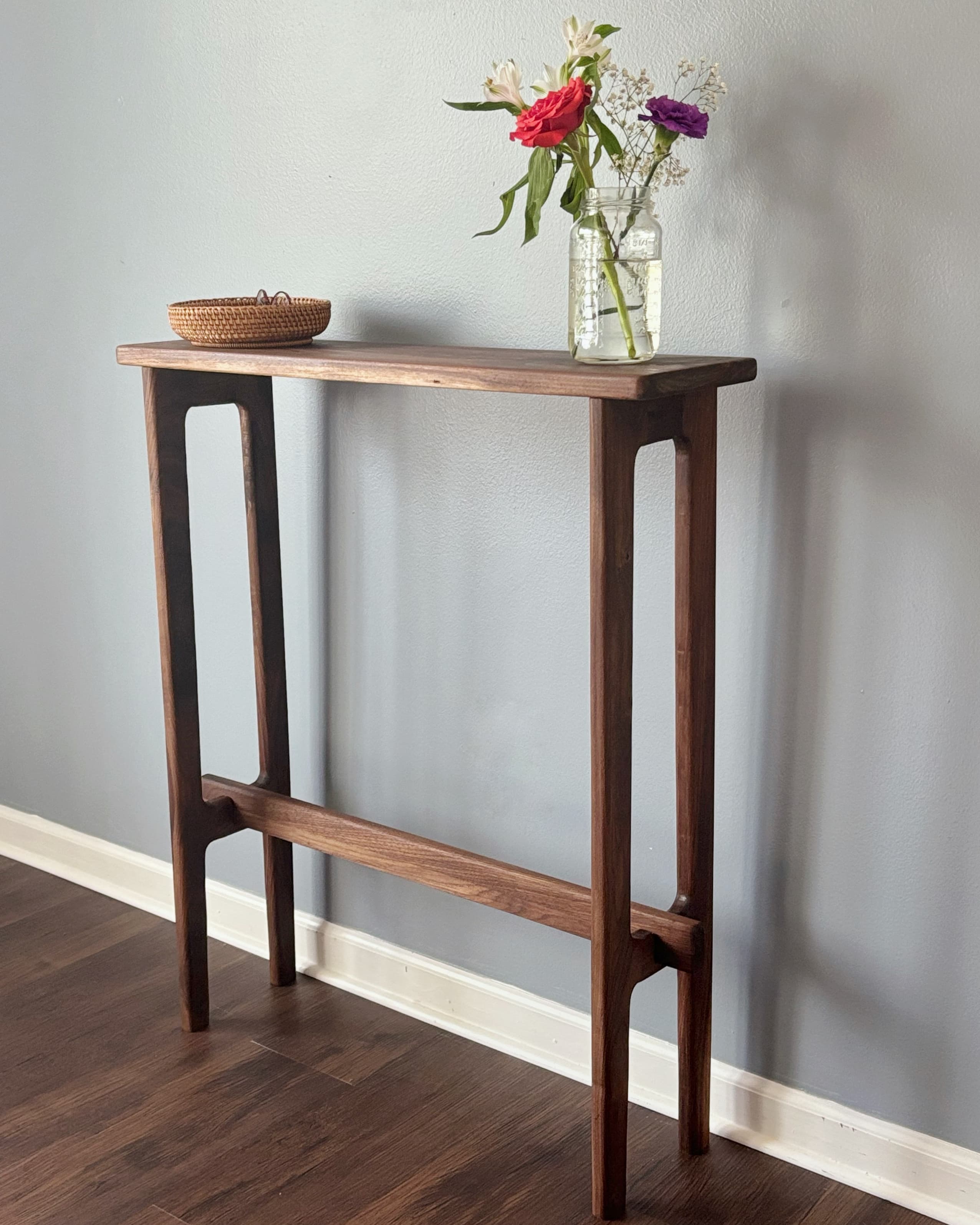 A minimalist, slimline console table crafted from dark walnut wood, featuring a rectangular top and integrated leg structures connected by a horizontal stretcher bar. — 3D model