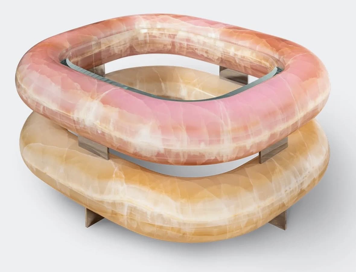 A contemporary coffee table featuring a distinctive toroidal design. The table consists of two stacked, interconnected torus-shaped structures, each appearing to be carved from translucent stone with a marbled pattern. A clear glass surface is integrated within the upper torus, creating a functional tabletop. The structures are supported by minimalist metallic or wooden legs at four points. — 3D model