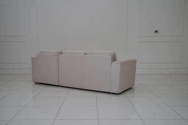 A sectional sofa with a chaise lounge extension, upholstered in a light-colored fabric with a subtle pattern. The sofa features three seat cushions and a chaise on the right side. It includes four matching throw pillows. The sofa has a modern, minimalist design with clean lines and low-profile arms and back. — 3D model