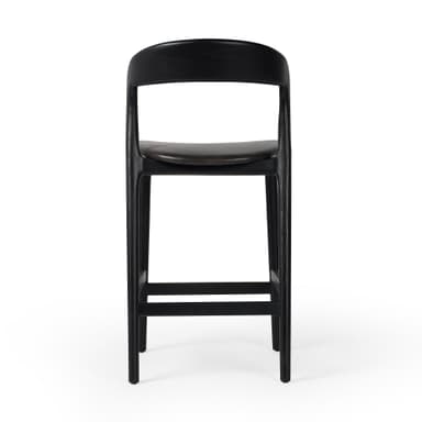 A contemporary bar stool with a black wooden frame and a dark upholstered seat. The stool features a gently curved backrest and a square footrest connecting the tapered legs. — 3D model