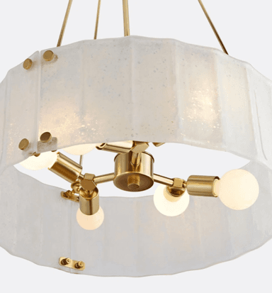 A close-up view of a modern chandelier featuring a circular arrangement of multiple exposed bulbs within a distinctive textured glass shade. The frame and bulb sockets are made of polished brass. The translucent glass shade has an irregular, possibly octagonal or faceted shape, and appears to be made of 'seedy' or artisanal glass, secured by visible brass fasteners around its upper edge. — 3D model