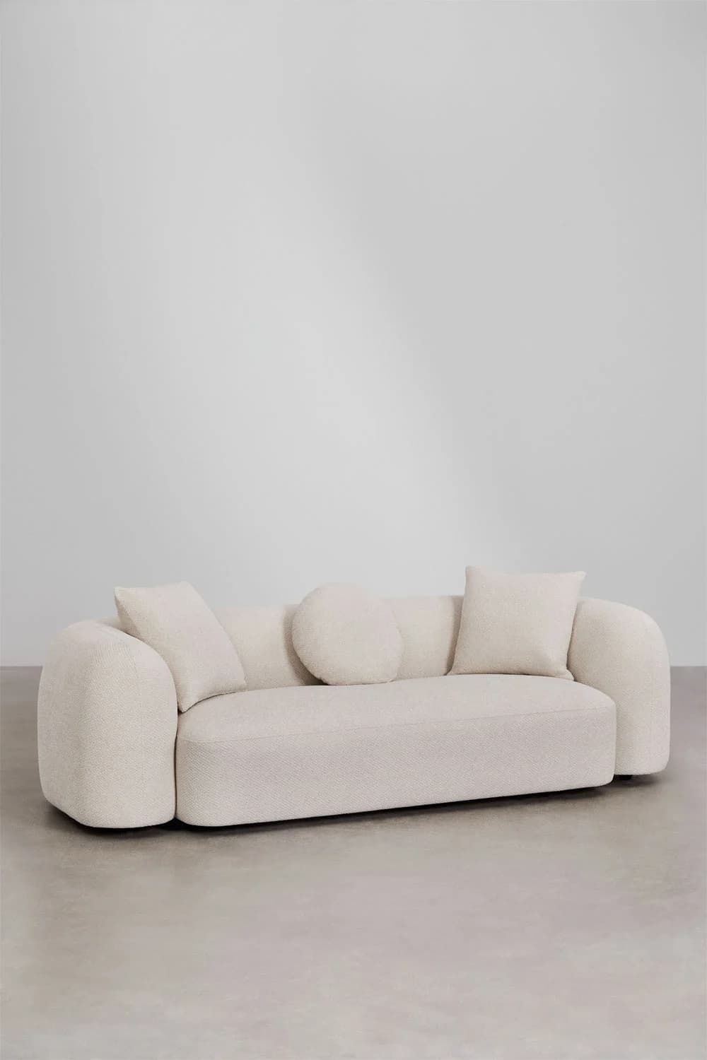 A plush, generously proportioned sofa with a rounded, organic form. It features deep seating and substantial, curved armrests. The upholstery has a textured boucle-like finish. The sofa is accompanied by several throw pillows, including two square ones and two circular ones, all in a matching fabric. — 3D model