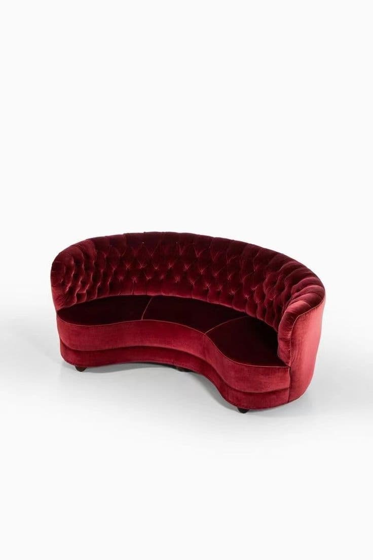 A luxurious curved sofa upholstered in deep red velvet, featuring a deeply button-tufted backrest and a continuous, low-profile design. The sofa has a graceful, serpentine form, devoid of prominent armrests, and rests on small, discreet feet. — 3D model