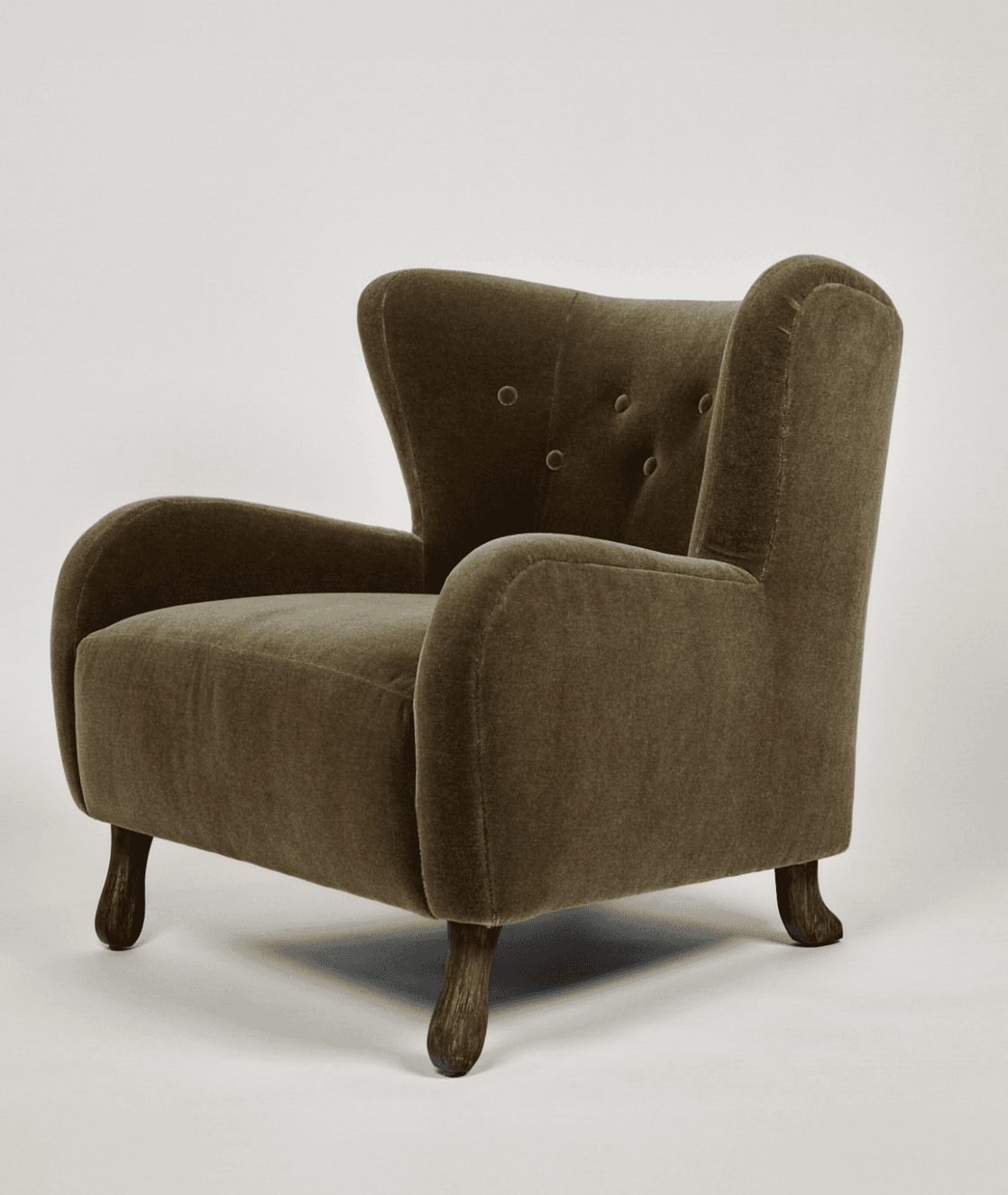 An upholstered wingback armchair featuring a high backrest with button tufting, gently rolled arms, and short, turned wooden legs. The chair is covered in a plush, textured fabric, possibly velvet or chenille, in an olive green hue. The overall design suggests a traditional or classic aesthetic. — 3D model